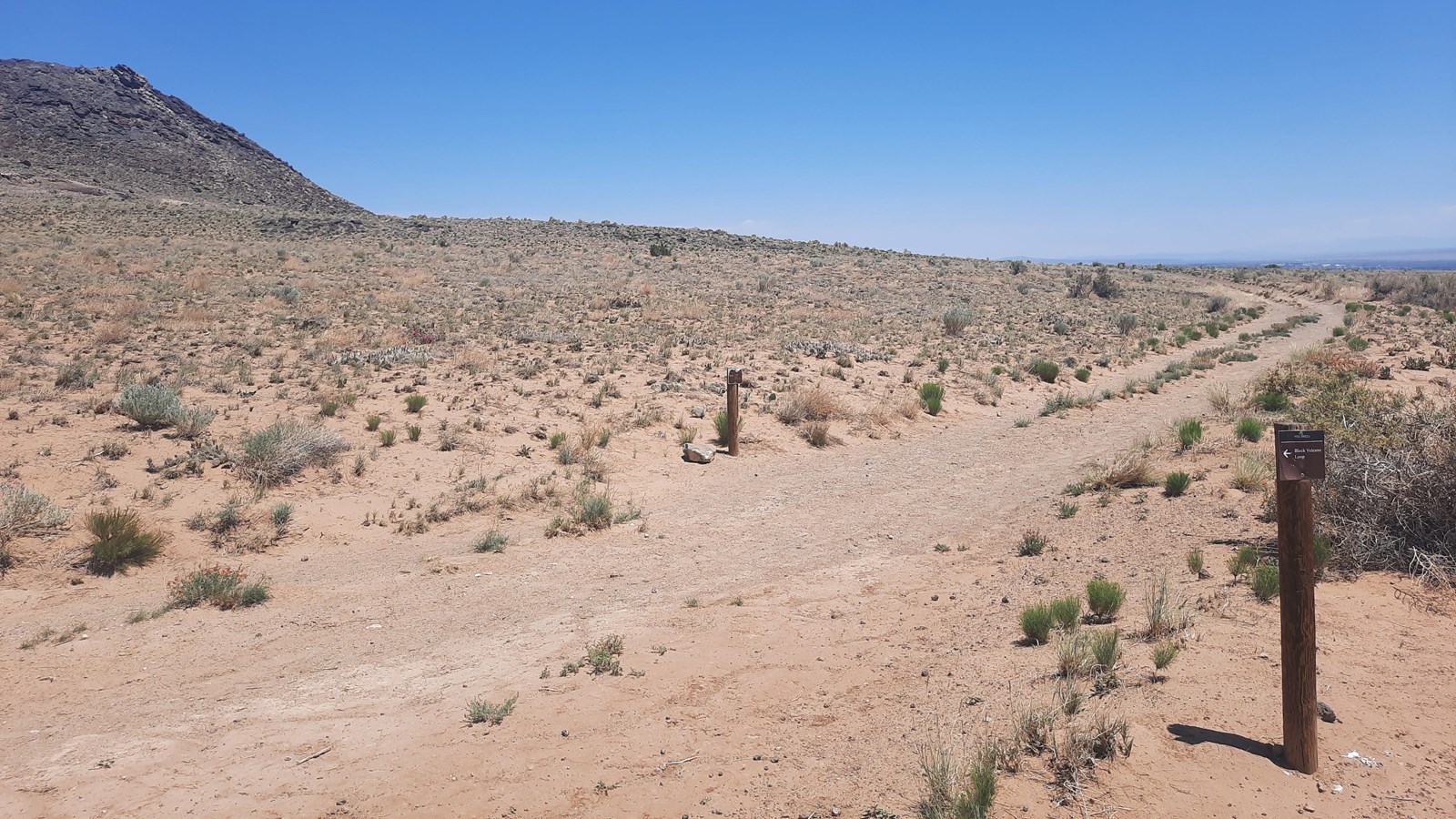 A trail going through an arid landscape with a volcano to the left.