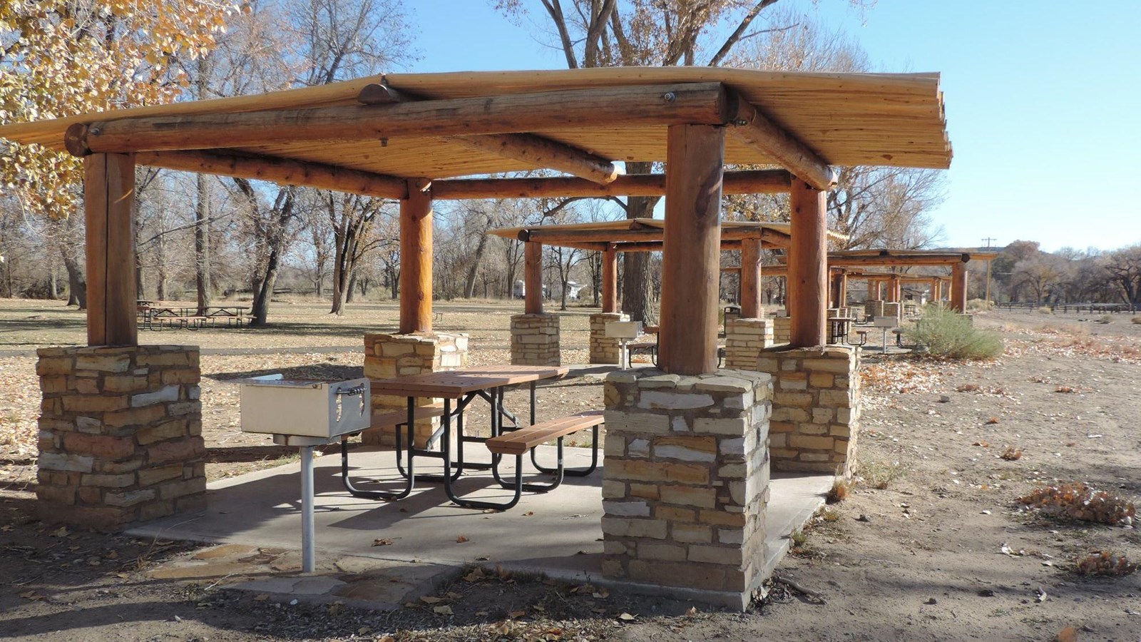 Photo of shade structure and picnic tables with a grill.