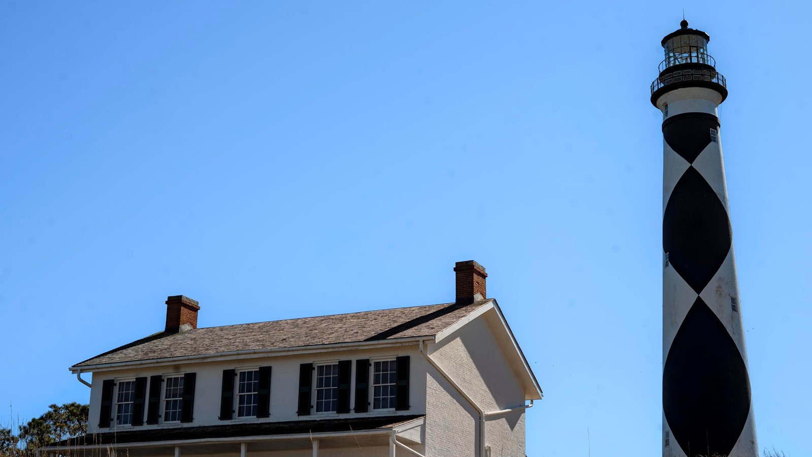 Cape Lookout Lighthouse next to Keeper\'s Quarters. Blue sky in the background.