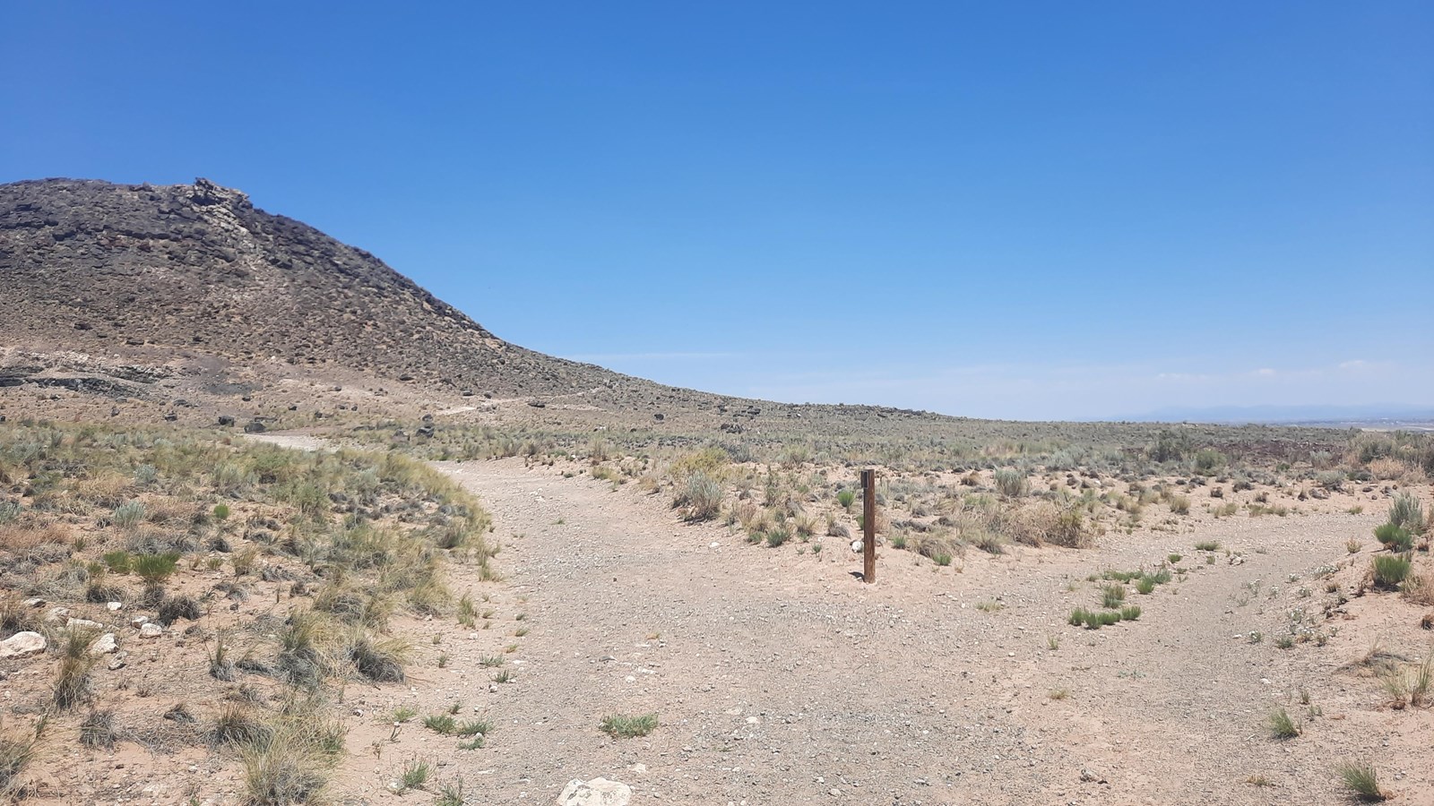 Fork in a trail through an arid landscape with a volcano to the left.