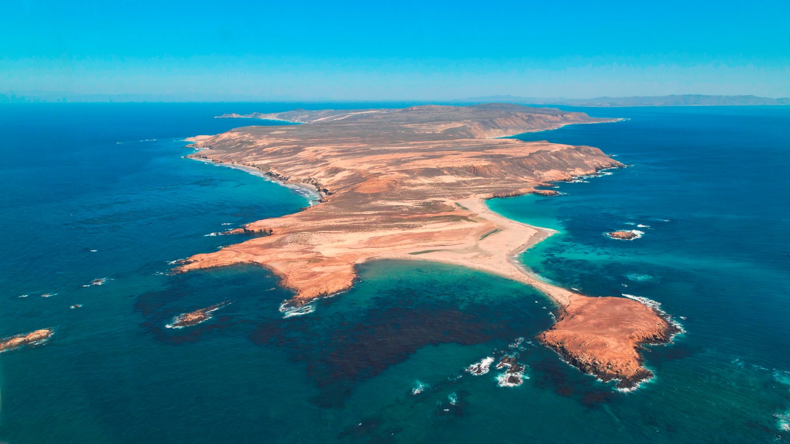 aeiral image of brown island with rugged coast and white beaches