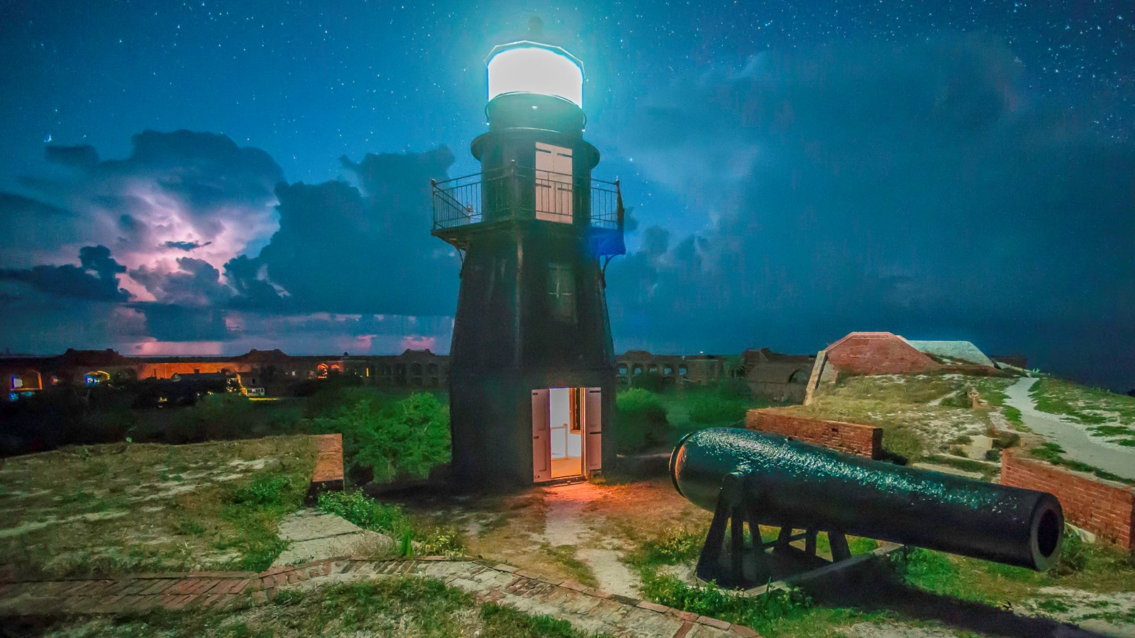 A night time view of the illuminated historic Tortugas Harbor Light with nearby parrot rifle cannon.