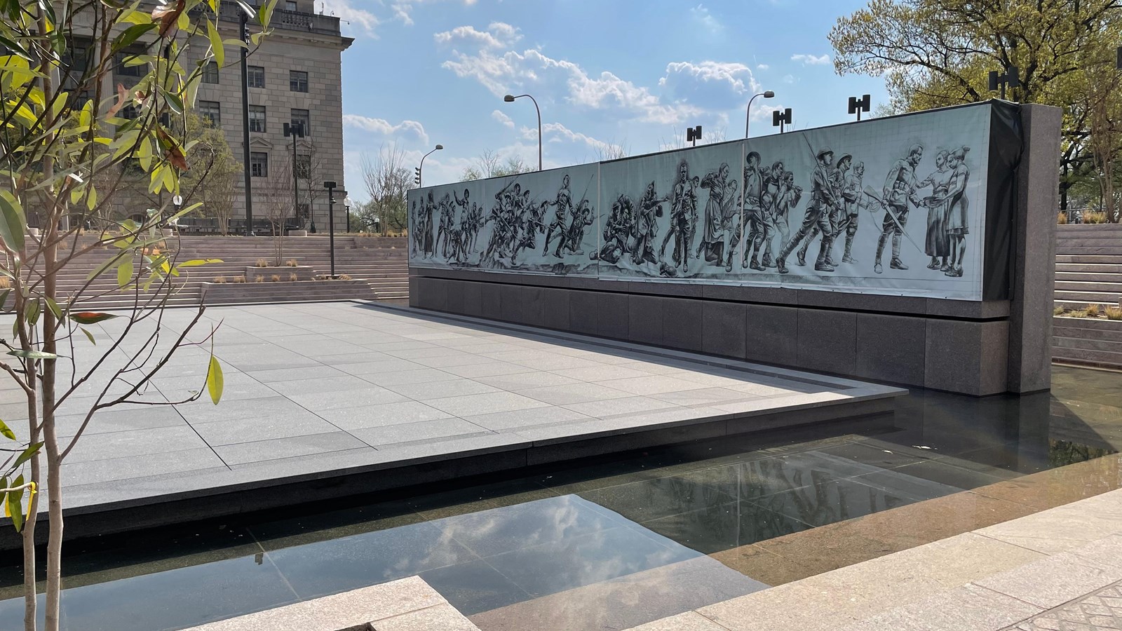 A rectangular pool in front of a stone wall with images of World War I soldiers.
