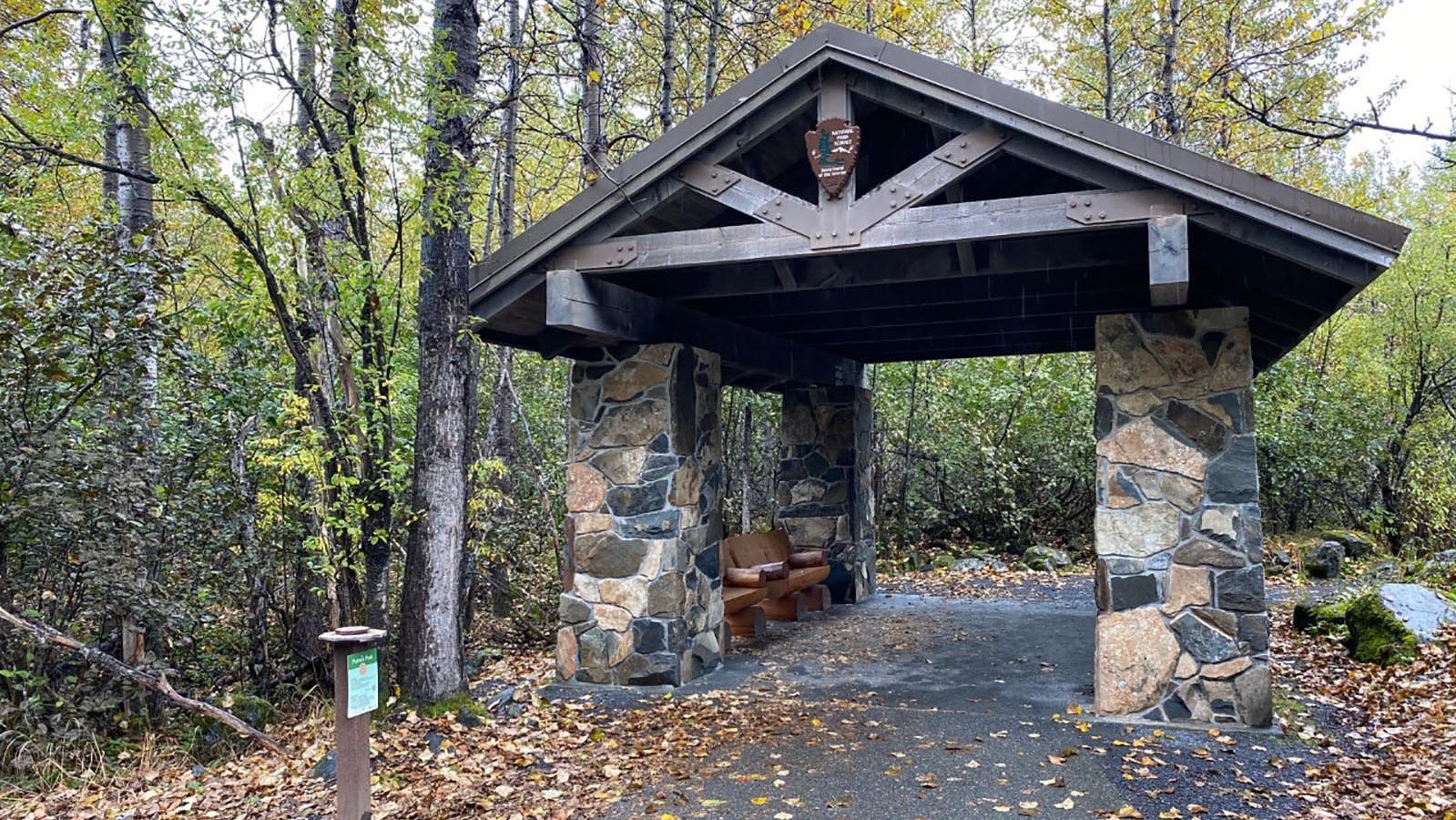 A stone building that goes across a path in a forest. There are benches under the structure.