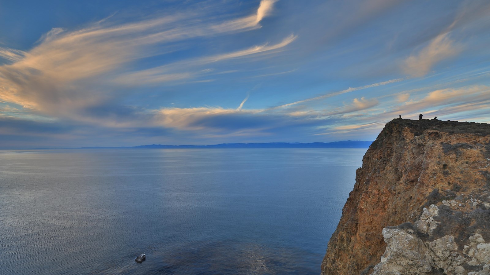 visitors standing on high ocean bluff watching sunset