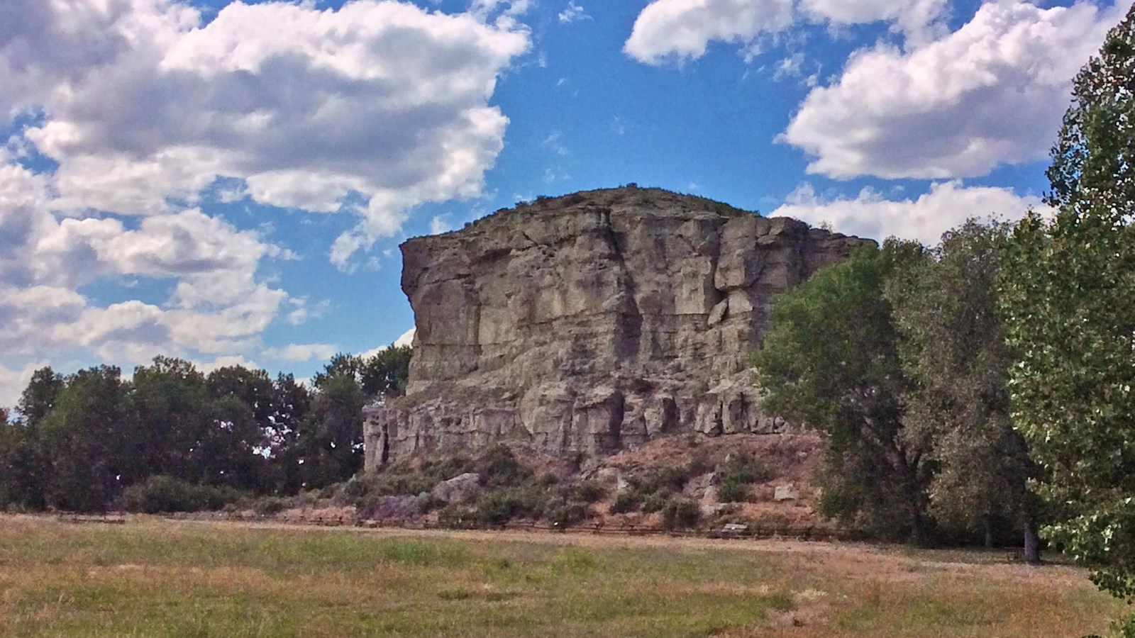 Large rock cliff rising from flat grassy surface