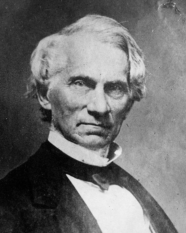 black and white image of a man wearing a bow tie and black jacket, facing the camera