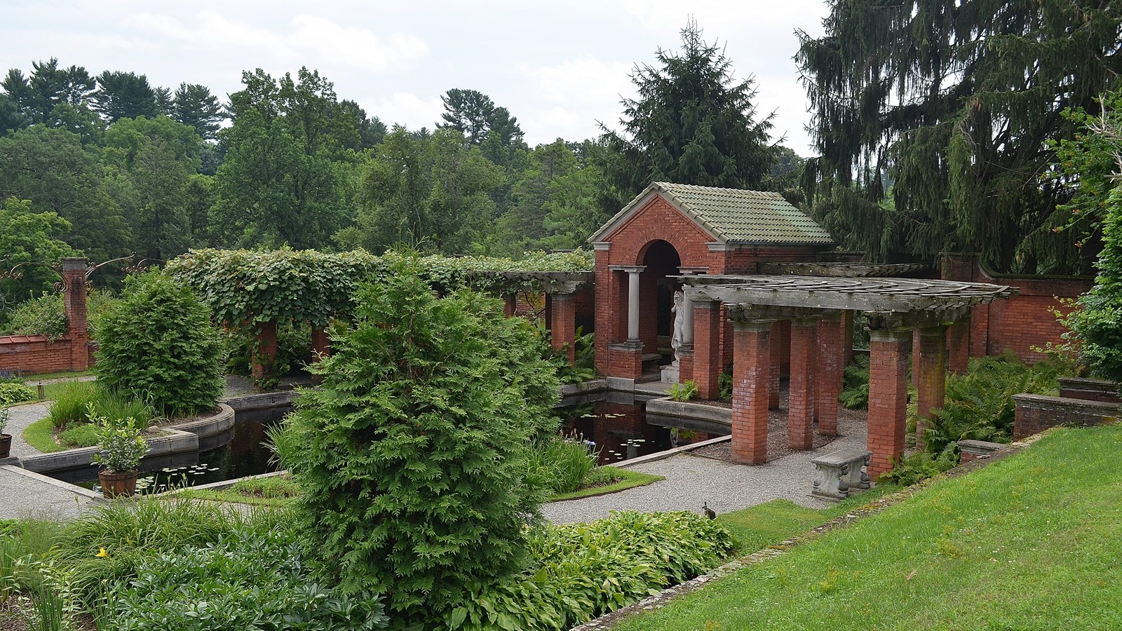 A lush green lawn with a brick pergola and reflecting pool.