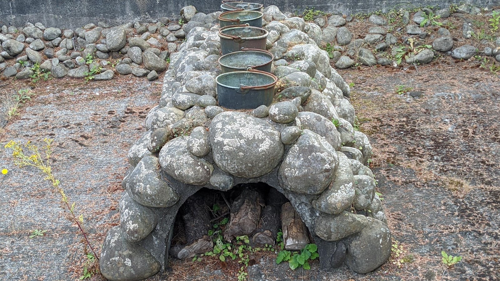 Various sized round stones connected to form a short arch support 5 kettles on top with wood inside