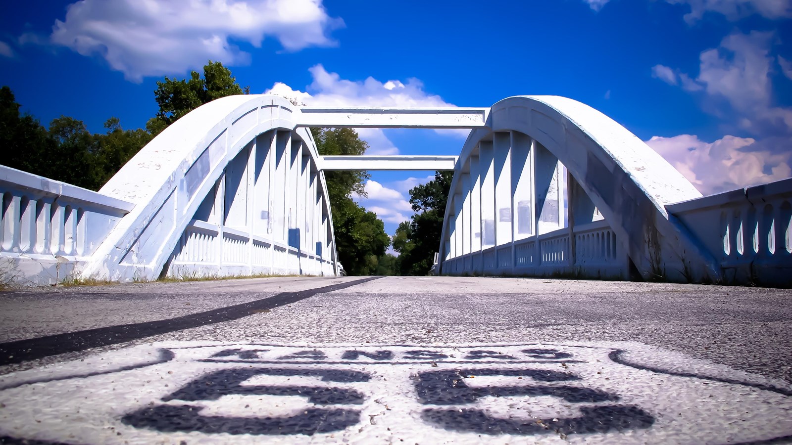 A white bridge with two large arches on either side with vertical beams inside the arches. 