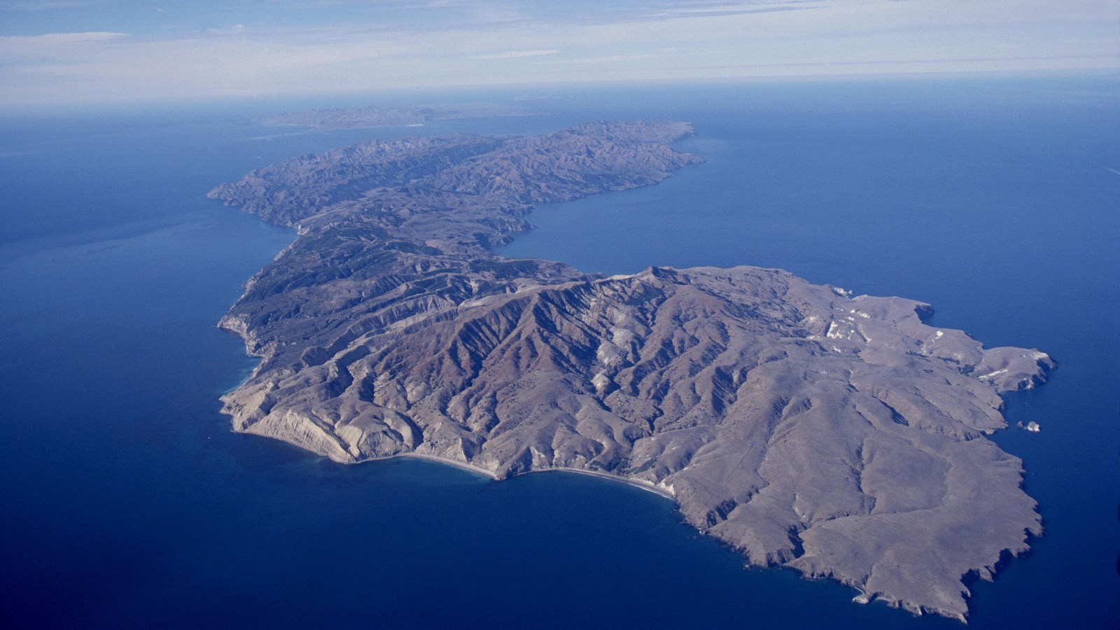 Aerial photo of long skinny island in blue sea.