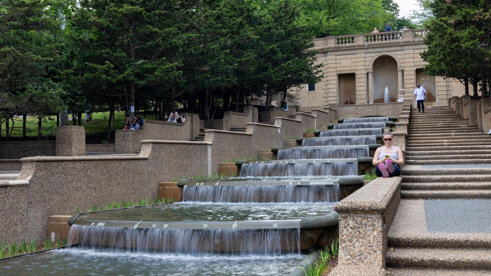 People sit and walk by a cascading waterfall flanked by stairs.