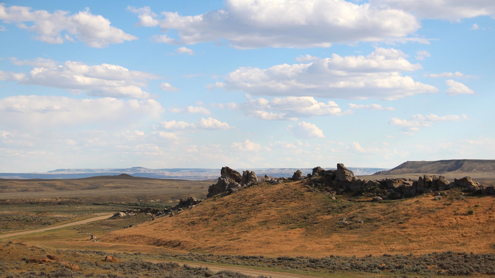 Steep grassy slope with jagged rock ridge under blue sky and scattered clouds.