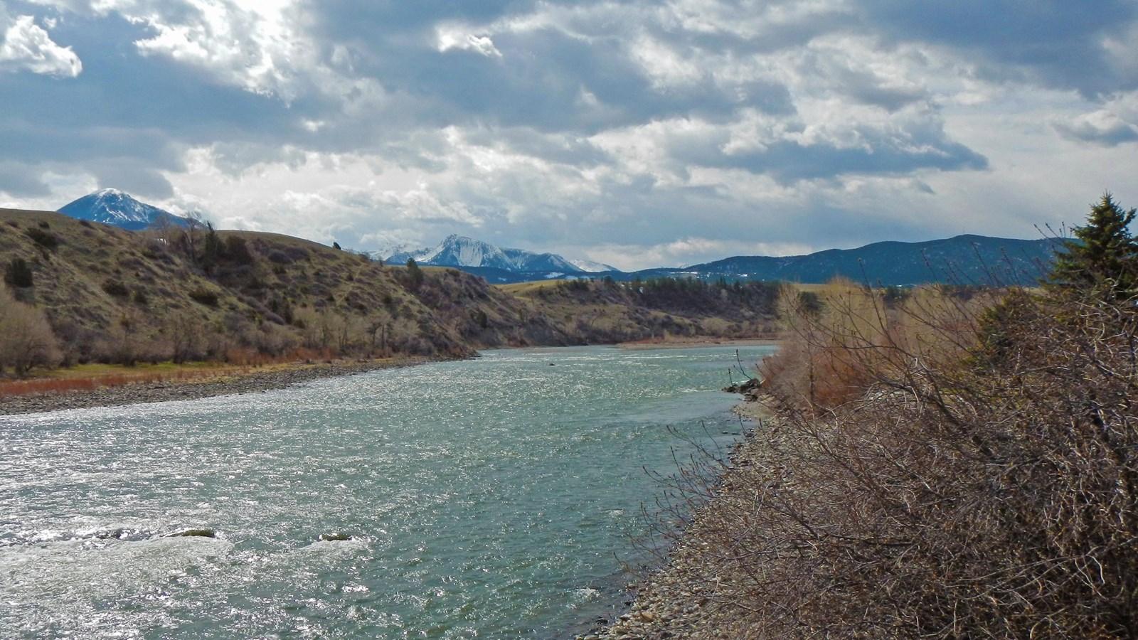 Large blue river with white capped mountain peak in the background