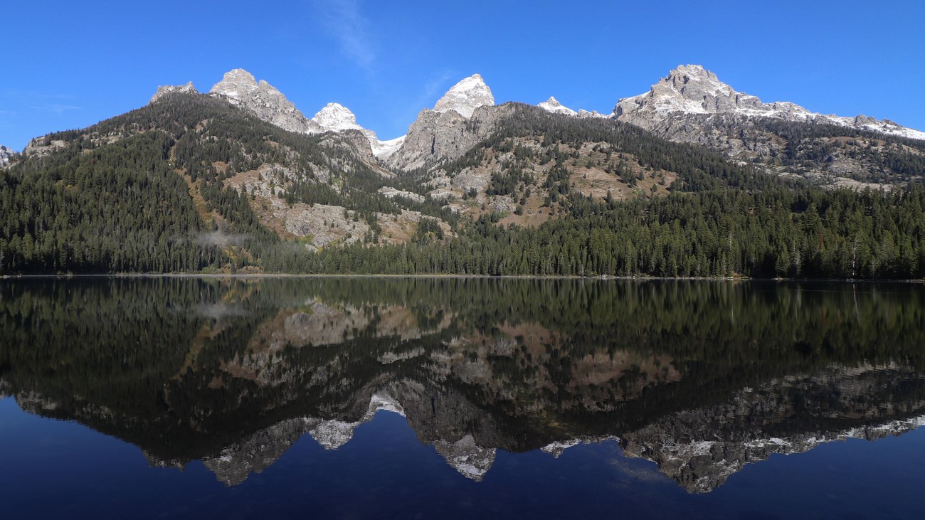 A lake sits at the base of a mountain range with a near perfect reflection on its calm surface.