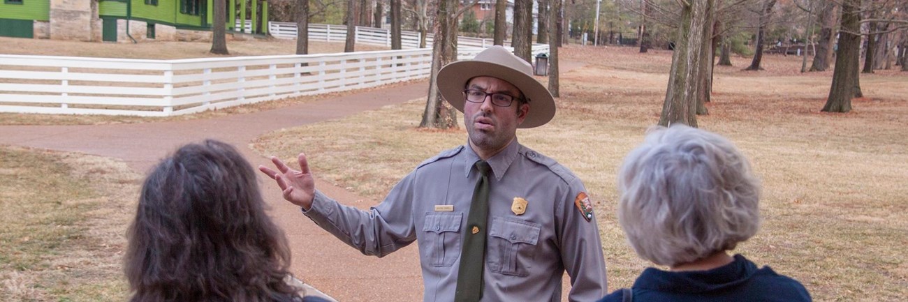 Park Ranger standing in front of a group of people with a green house in the background.