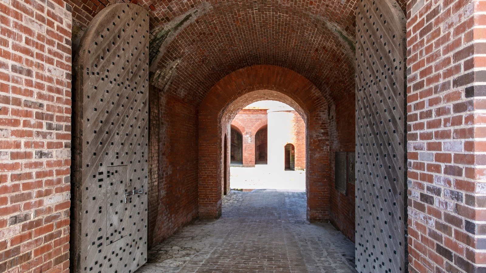 Large wooden doors swing open in a red brick fort.