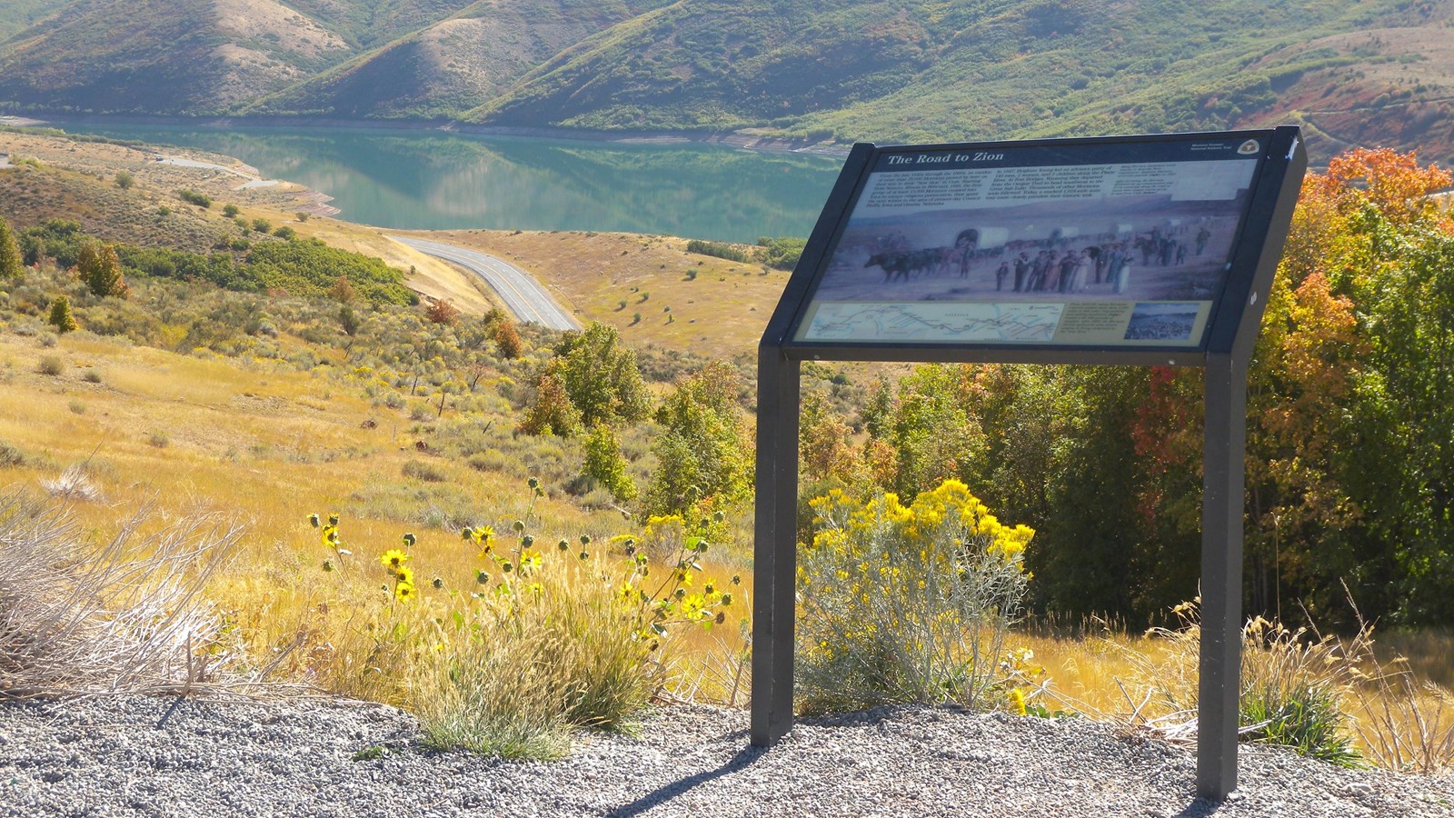 An exhibit panel sits in front of an expansive mountain valley view with a distant lake.
