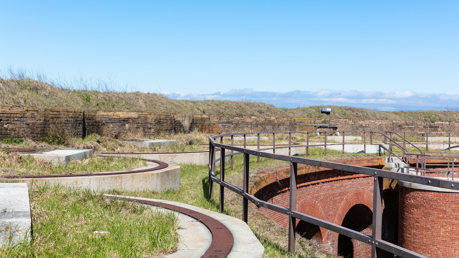 A metal handrail guards a grassy edge at the top of a fort.