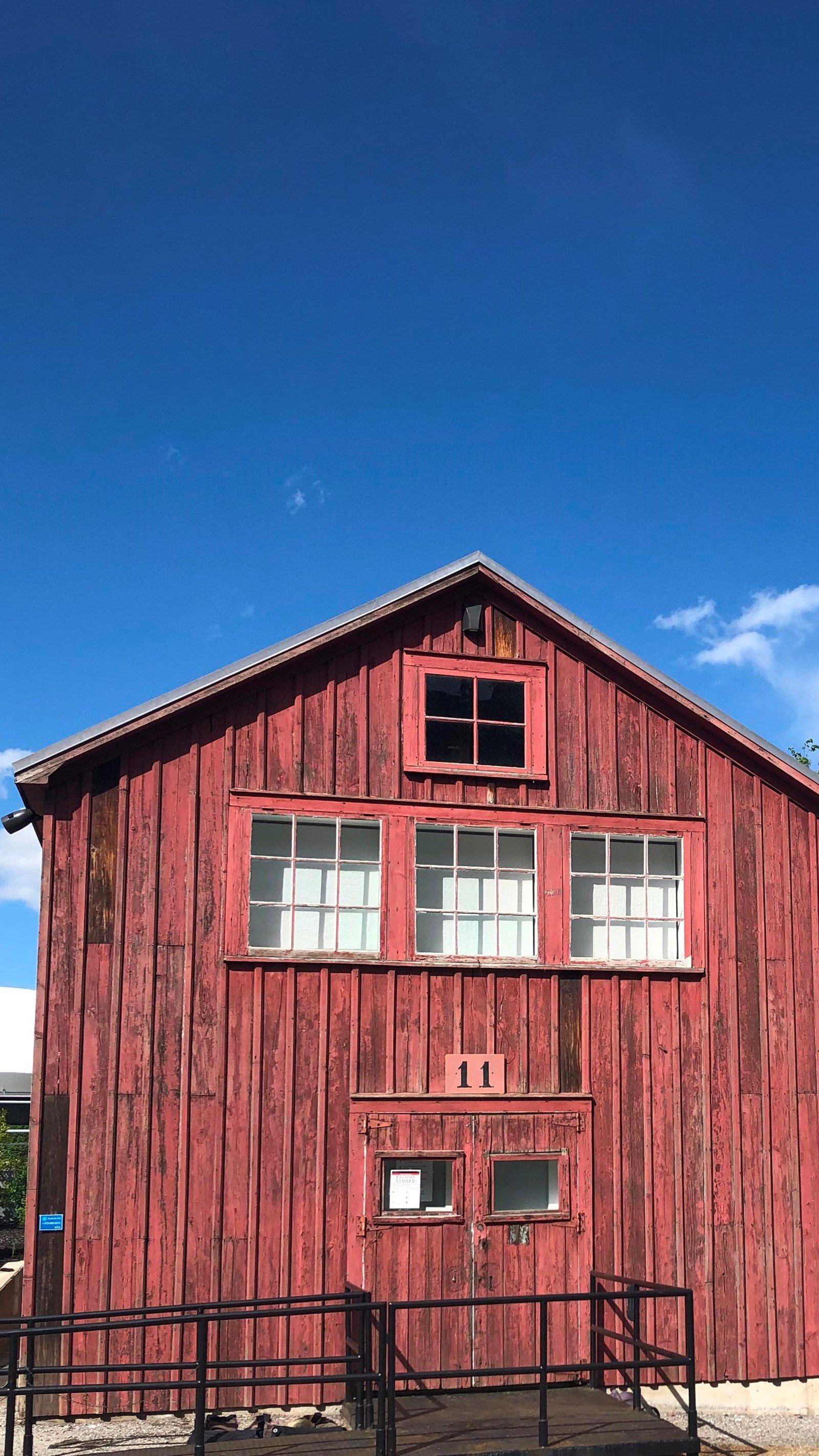 Exterior of red wooden building, with a sign painted with a number 11 over door. Blue sky.