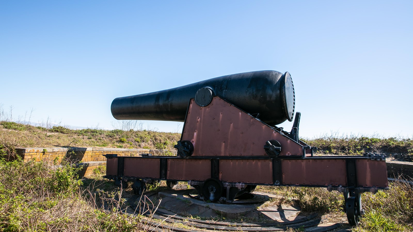 A large cannon peers over the wall on top of a grassy fort.