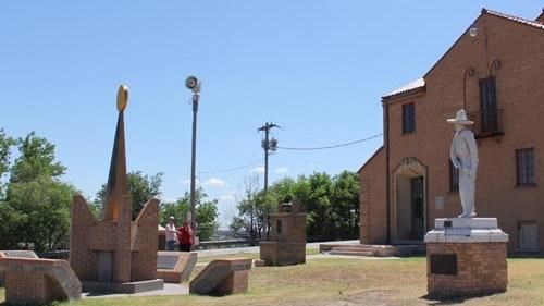 A cowboy statue and obelisque statue in front of an old brick building.