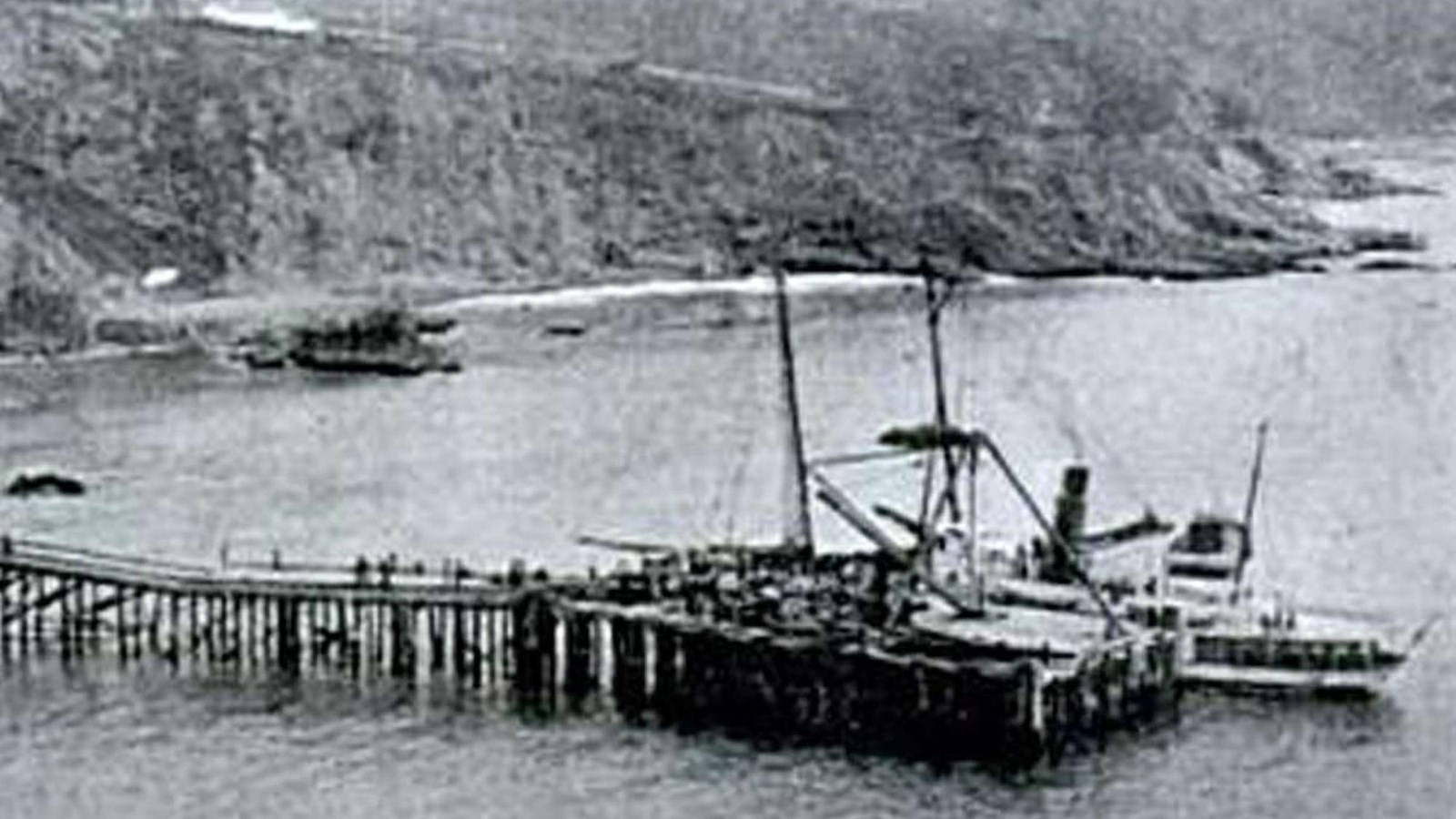 Black and white image of a dock with cranes extending out from a cove. 