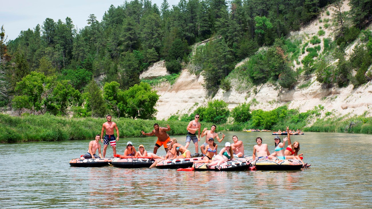a collection of 7 tubes on the river, with 13 people floating on them; they are tied together.