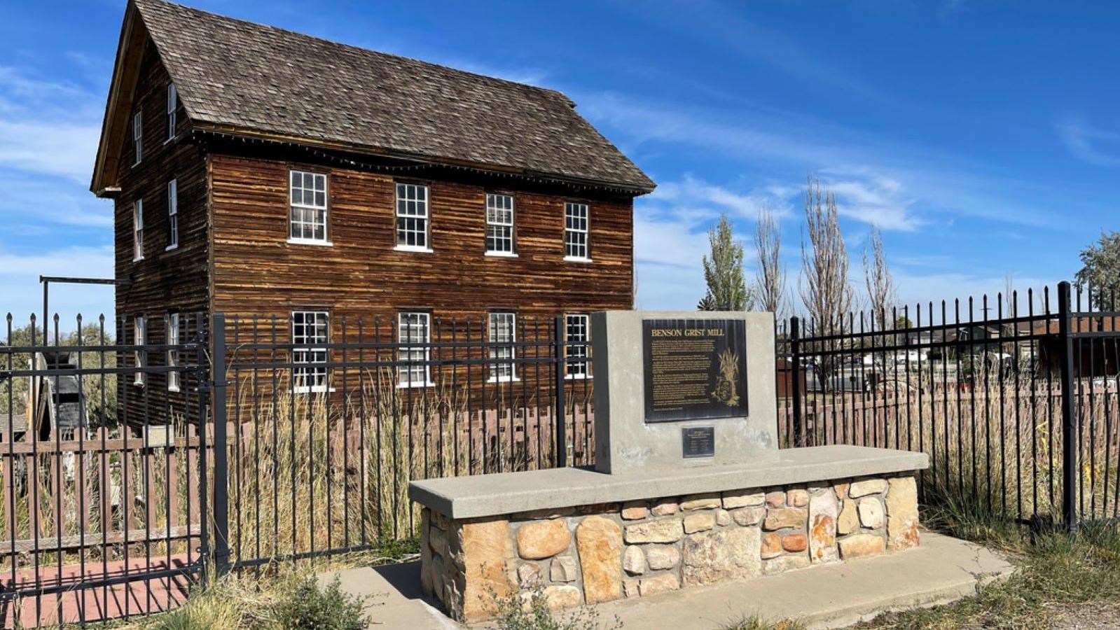 A plaque sits in front of fence and 3‑story Benson Grist Mill under a blue sky.