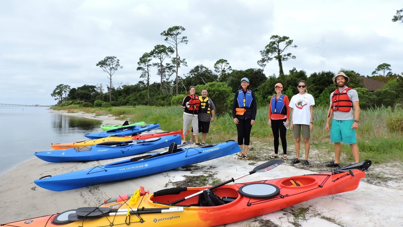A group of kayakers stands on the seashore.