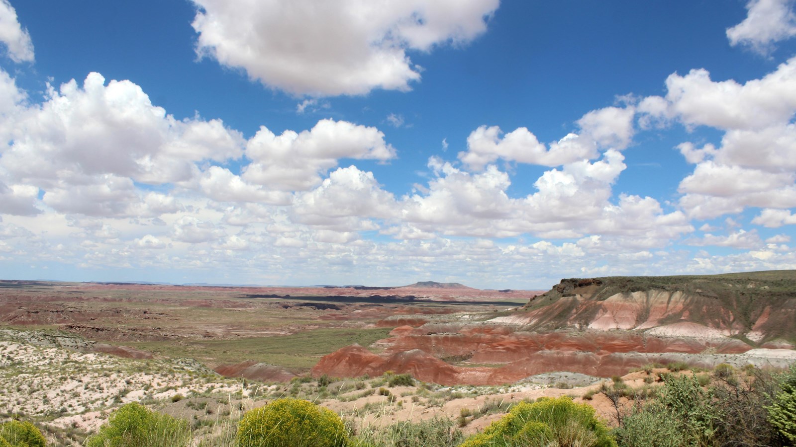 Red badland topography under a mostly sunny sky.