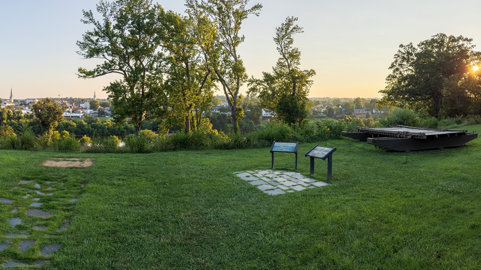 A terraced lawn with a pontoon bridge and interpretive signage looking over a river.
