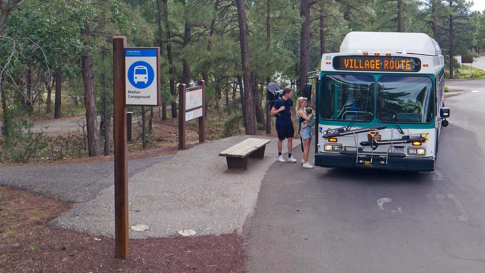 as an open air bus stop, two people are boarding a white and green bus.