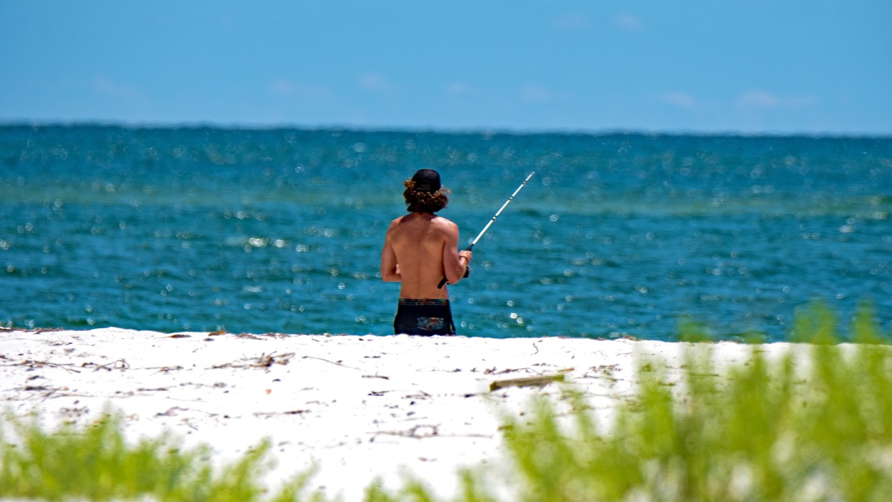 A fisherman stands with his line in the Gulf.