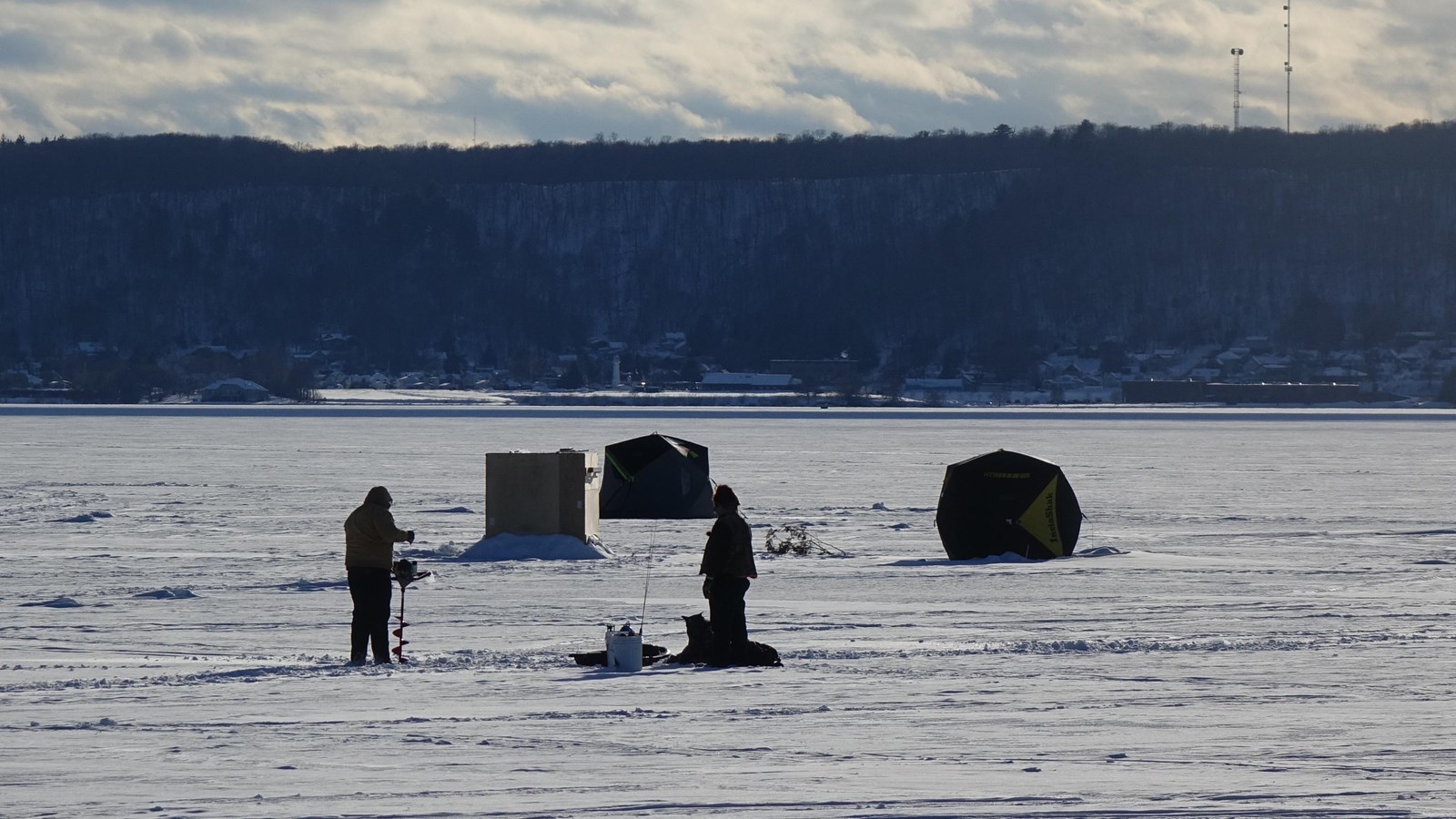 Several ice fishing shanties on Munising Bay with hills in the distance.