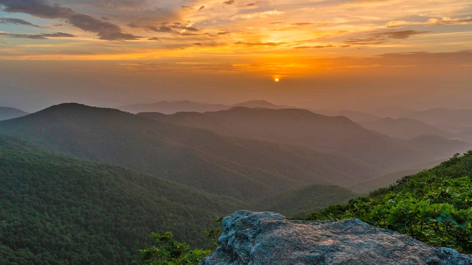 A hazy sunset over the lush, green, forested mountain.