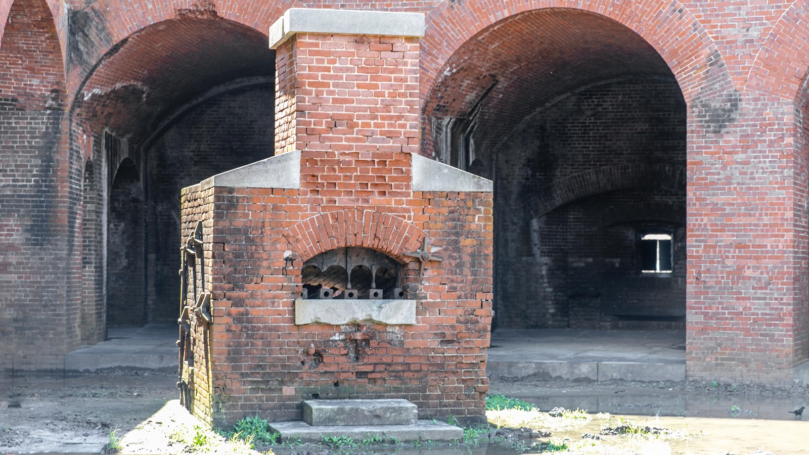 A red brick furnace stands near archways in a fort.