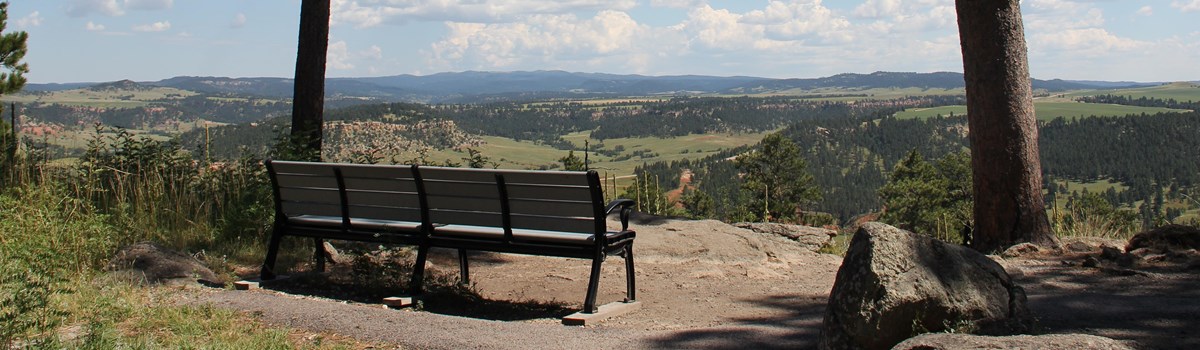 A bench along a trail overlooking a valley.