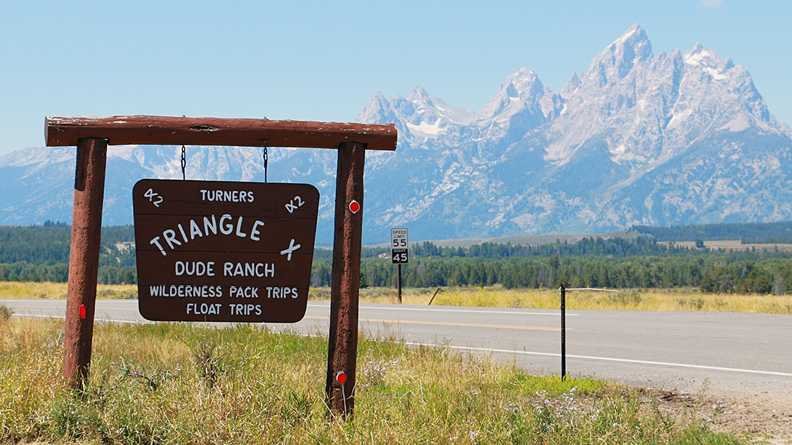 A wooden sign with the ranch name with the Teton range in the background.