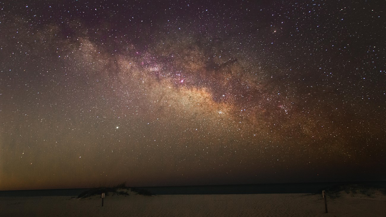 A night sky full of stars and the Milky Way shines over the beach.