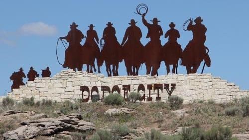 A silhouette of people on horseback on top of a rocky outcropping.