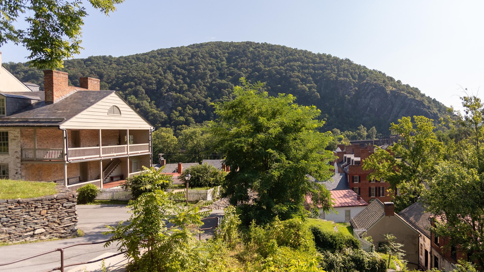 A house with a two-story balcony at the top of a hill overlooking a valley with trees and buildings.