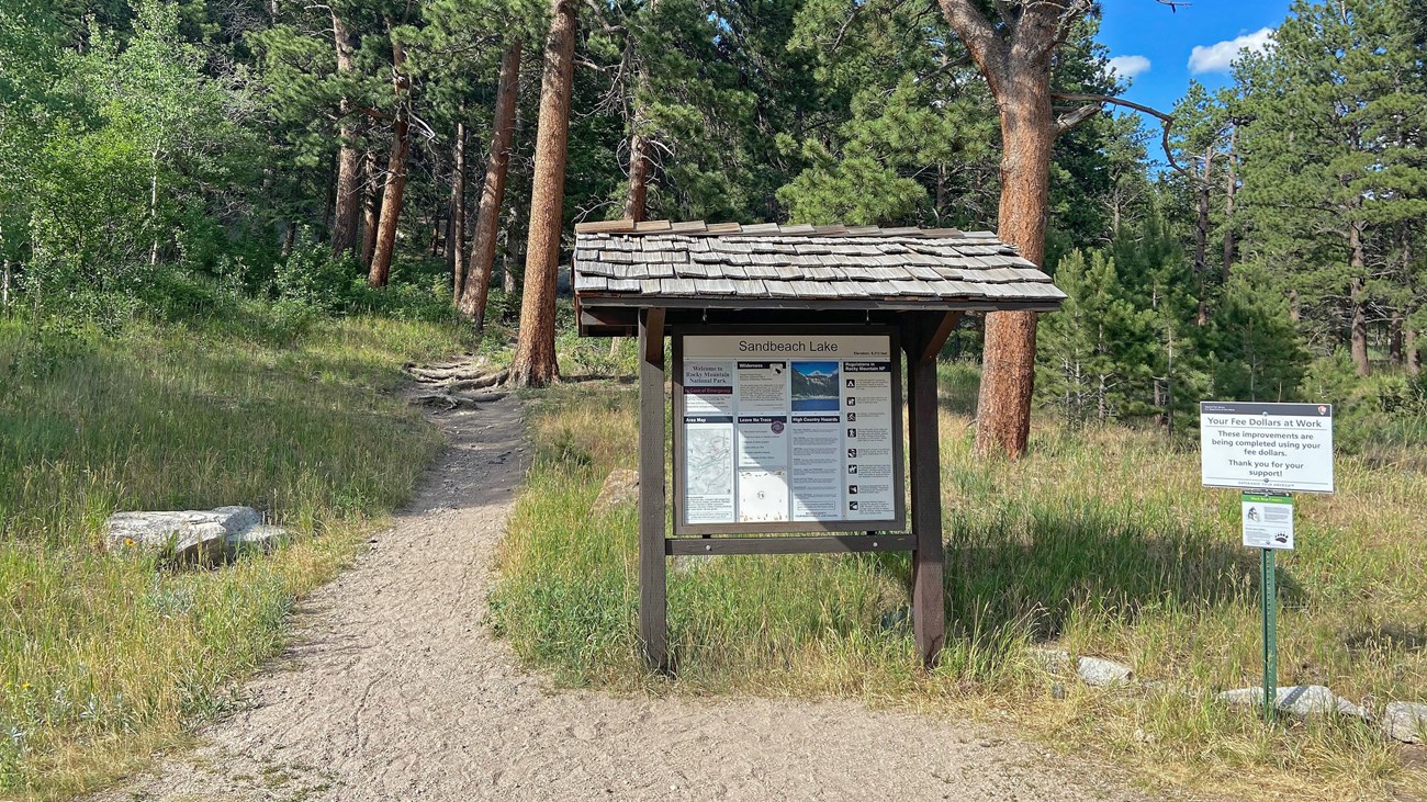 View of the Sandbeach Lake Trailhead. The trail is located to the left of the bulletin board.