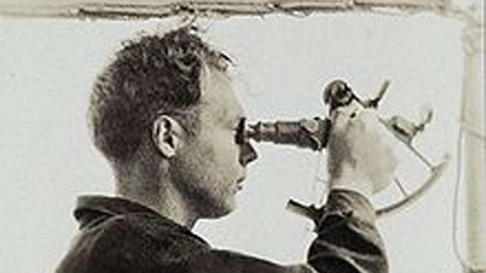 Black and white image of a man using a sextant. 