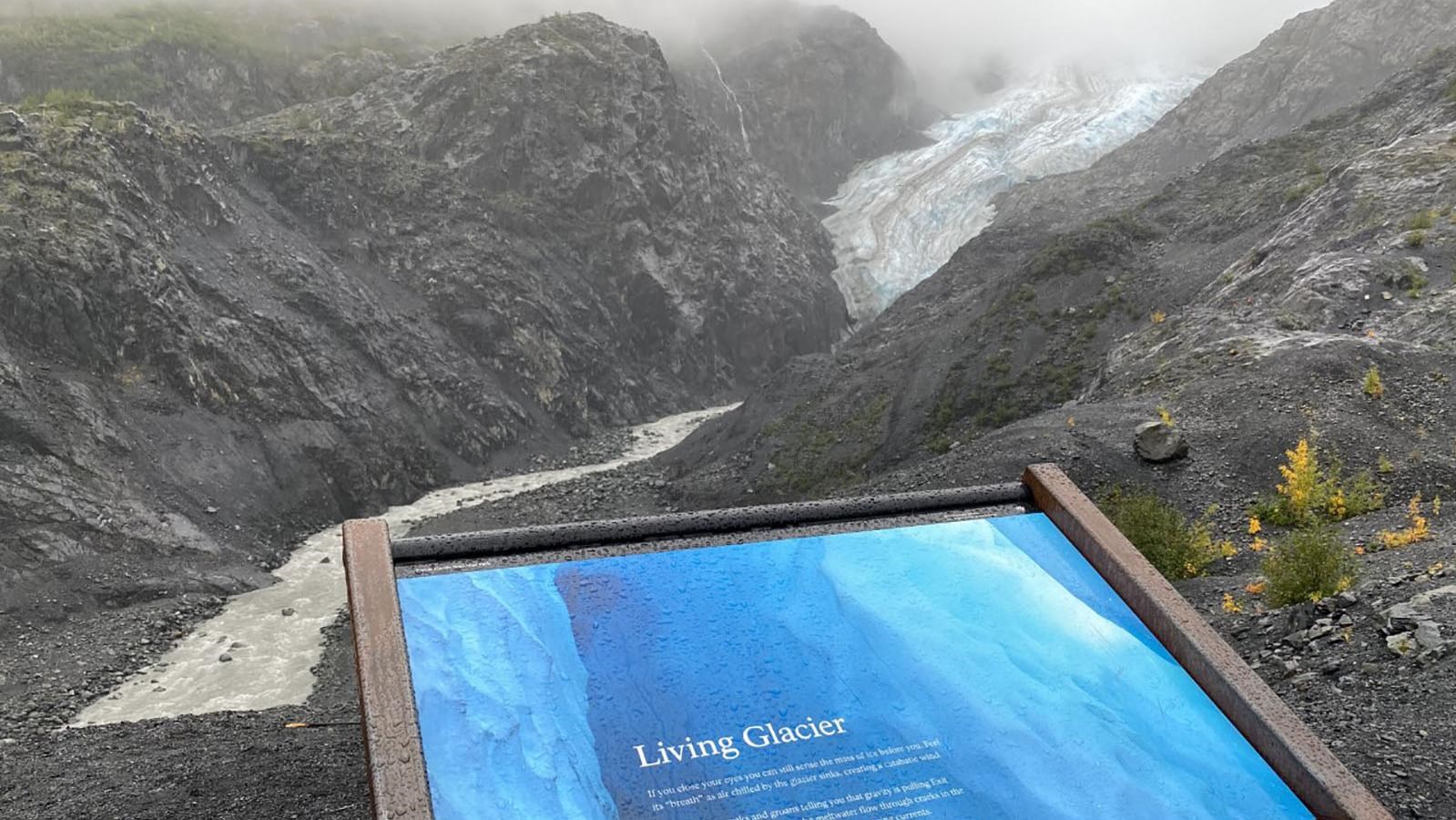 An interpretive display is in the center. In the background is a glacier between two mountains.