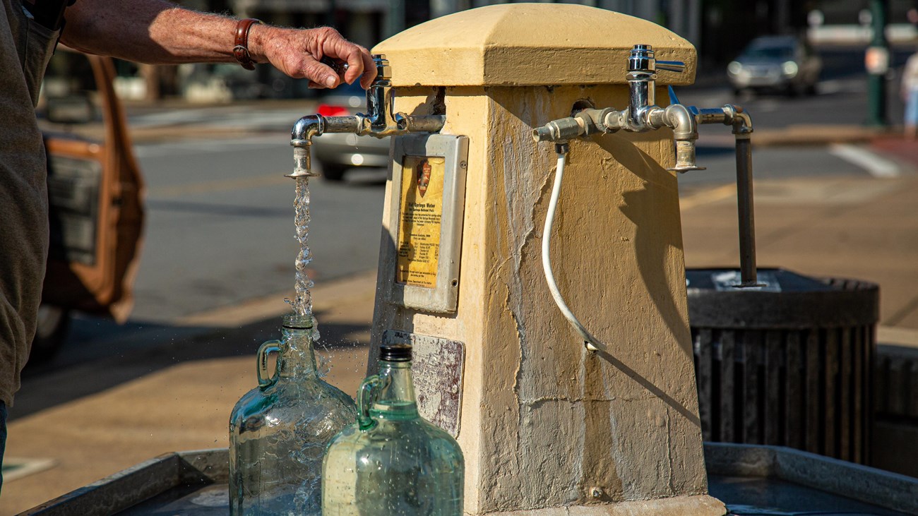 Person filling up glass water jugs.