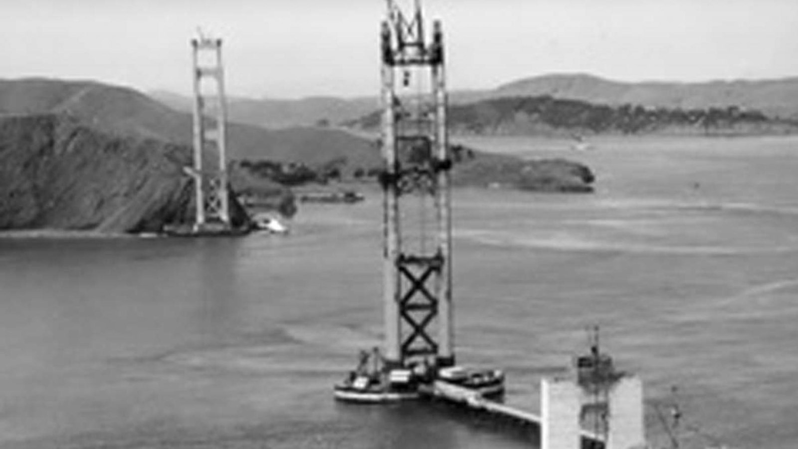 Black and white image of towers being constructed in a wide channel to support a future bridge. 