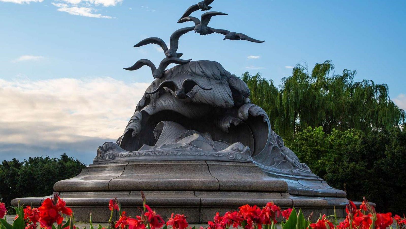 Statue of waves and seagulls surrounded by red flowers