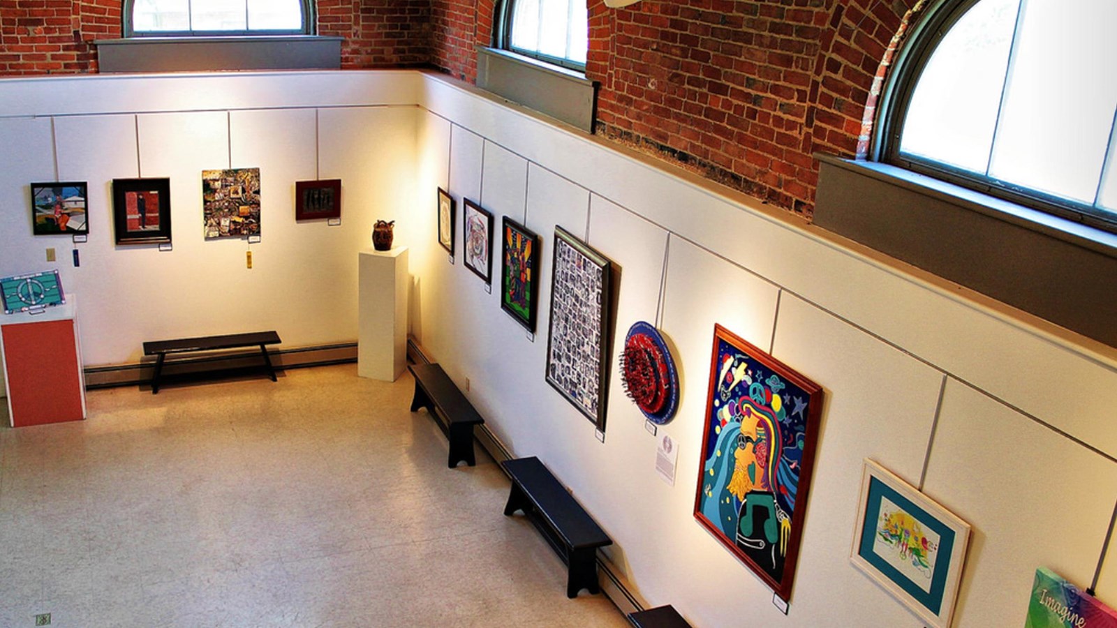 Walls full of artwork hanging from a rail on the wall and brick walls above the artwork