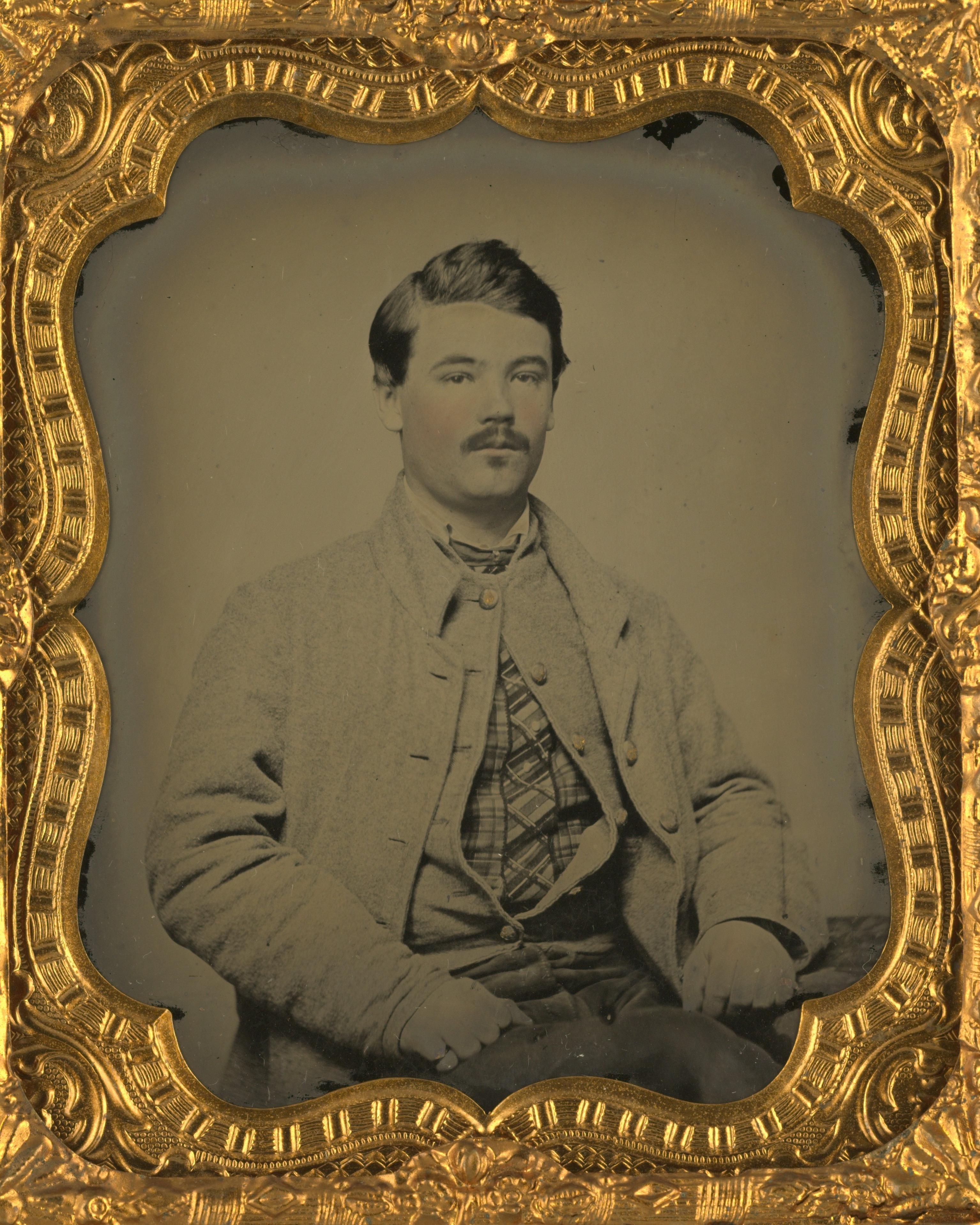 A Civil War era seated portrait photo of a pudgy young man is displayed in a frame within a case. 